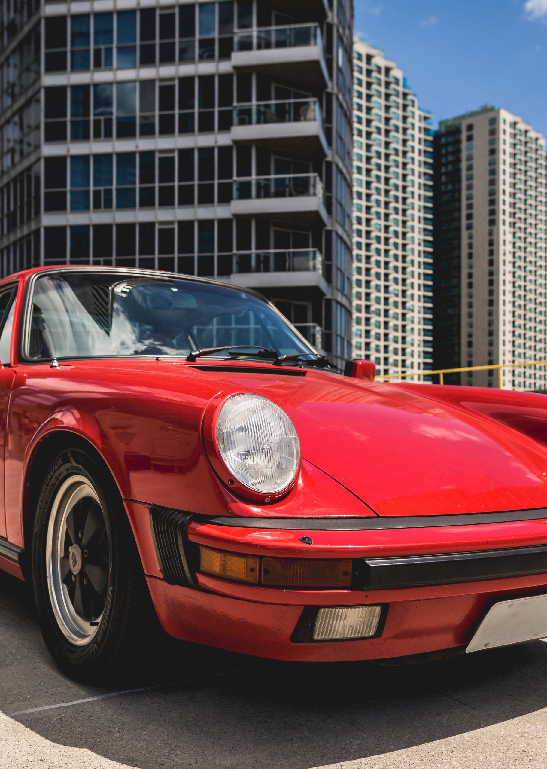 "Red Porsche parked in front of high-rise buildings, promoting custom installation services for luxury vehicles"